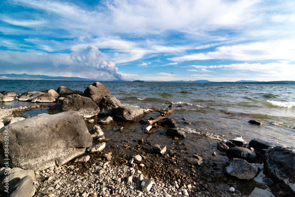 Obraz premium Large rocks on the banks of Yellowstone lake in Wyoming with a large wildfire in the background