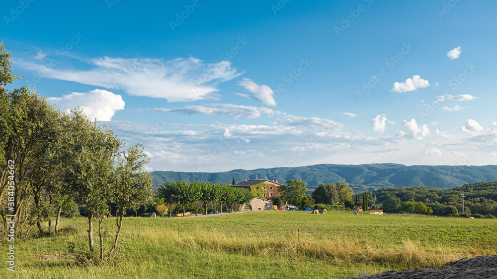 Green rural meadow landscape with rural farmhouse on a blue sunny sky