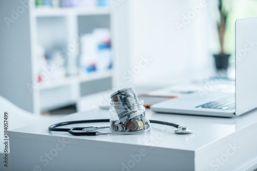 Jar with coins and stethoscope near the laptop