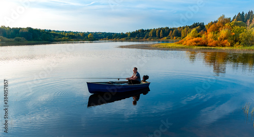  Elderly man fishing with a rod on a small fishing boat on the lake at autumn sunset