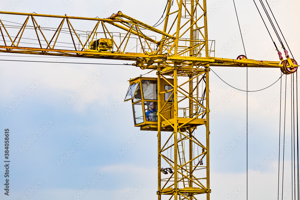 Partial view of a yellow tower construction crane - Operating cabin with operator inside it.