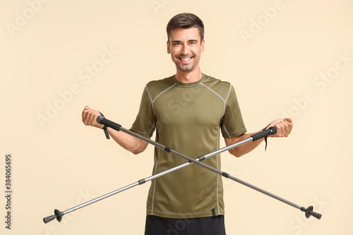 Young man with walking poles on color background