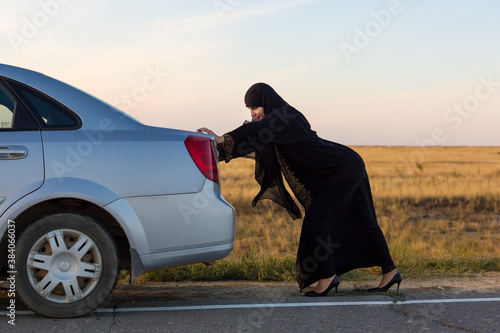 An Islamic woman is pushing a car along the road. Woman driver - car breakdown.