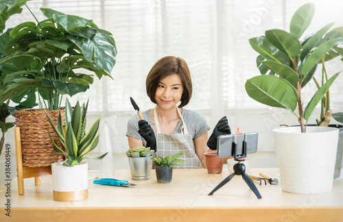 Portrait of young asian woman planting plant pot to fan channel, recording video at home. Online influencer girl in social media marketing live her hobby, lockdown coronavirus new normal quarantine.