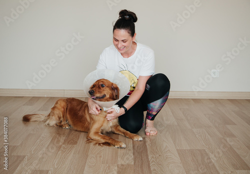 Young girl looking at her dog Golden Retriever with Elizabethan Plastic Cone. Medicine concept for pets.