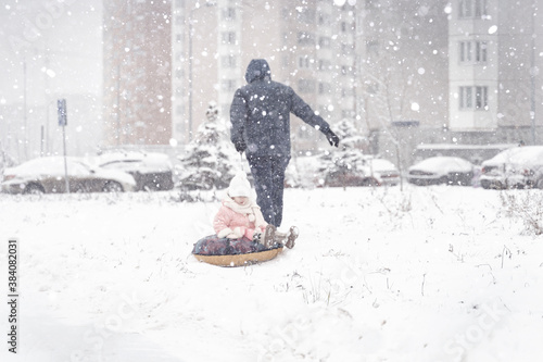 dad is taking his little daughter on a tubing in a heavy snow storm. focus on snow. people are out of focus. snow veil covers people
