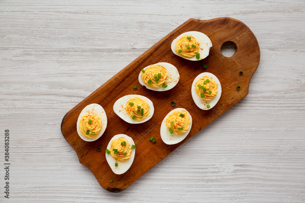 Homemade Deviled Eggs with Chives on a rustic wooden board on a white wooden table, top view. Flat lay, overhead, from above. Homemade Deviled Eggs with Chives on a rustic wooden board on a white wooden table, top view. Flat lay, overhead, from above.