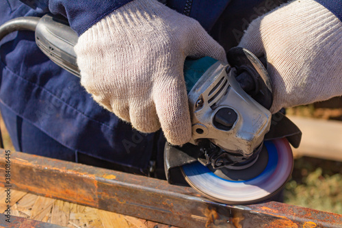 Canvas Print A worker in overalls is grinding a weld seam on a steel square profile pipe with an angle grinder with a flap disc