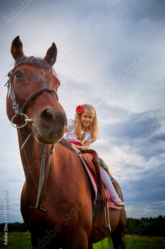 Girl in nice Gypsy dress with sorrel horse in a field with green grass and sky with clouds in background