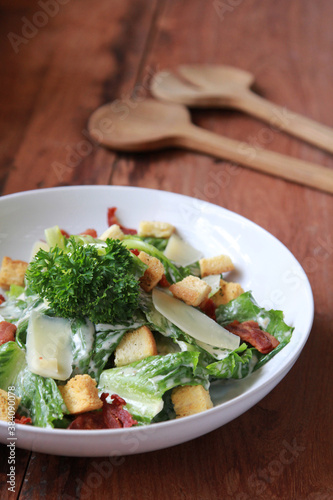 Close up Caesar salad with homemade croutons, sliced bacon, parmesan cheese and Caesar dressing in large ceramic white bowl.