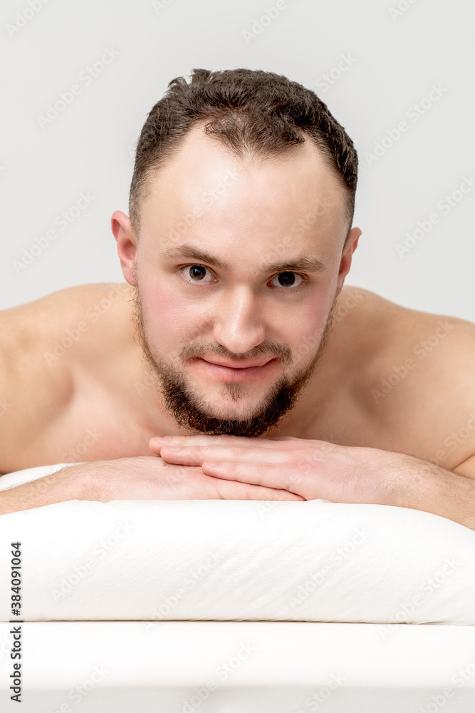 Obraz premium Young caucasian man lying on front on table spa, waiting for beauty treatment and looking at camera