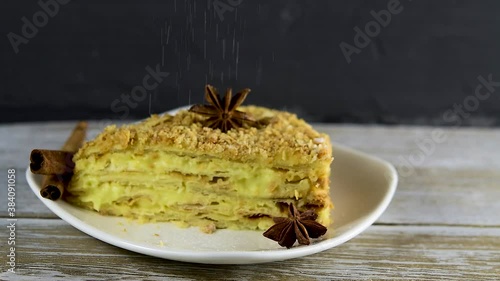 Piece, slice of Napoleon puff pastry with custard on a white plate on a wooden table close-up