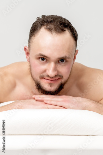 Young caucasian man lying on front on table spa, waiting for beauty treatment and looking at camera