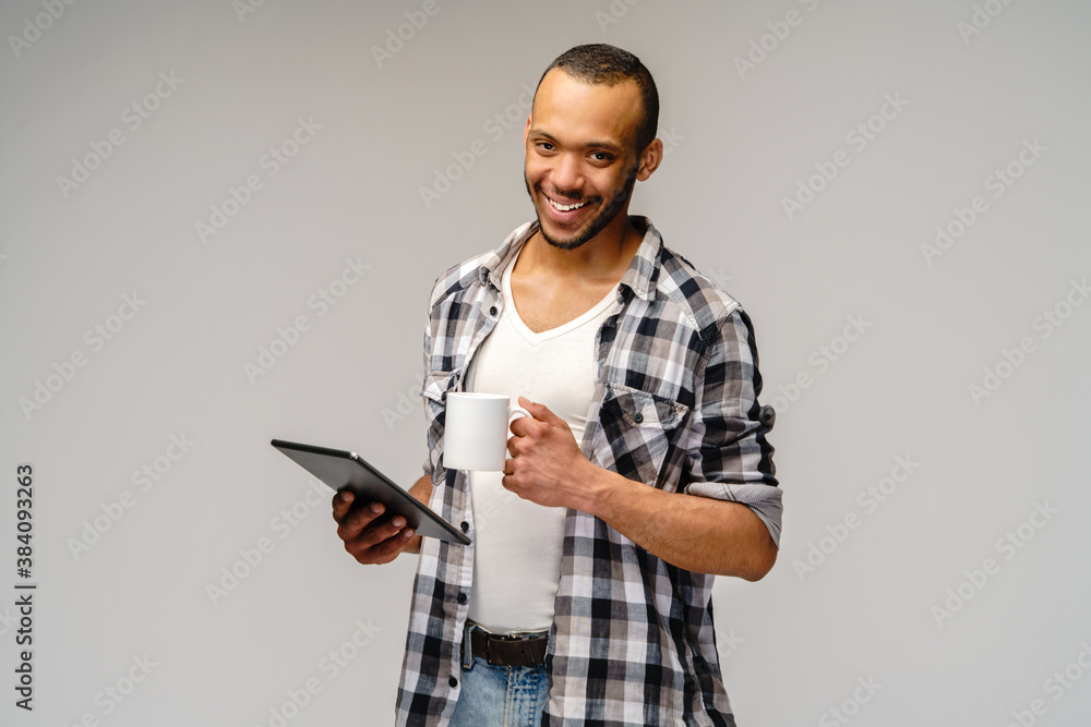 Portrait of a young african american man wearing casual shirt holding tablet pc pad and cup of coffee Portrait of a young african american man wearing casual shirt holding tablet pc pad and cup of coffee