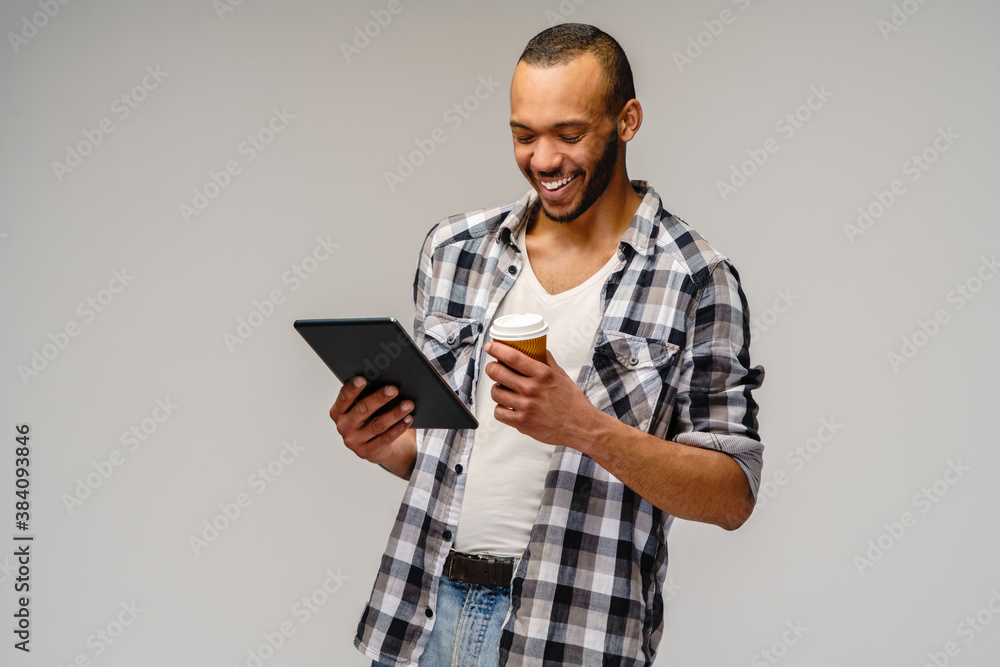 Portrait of a young african american man wearing casual shirt holding tablet pc pad and cup of coffee Portrait of a young african american man wearing casual shirt holding tablet pc pad and cup of coffee