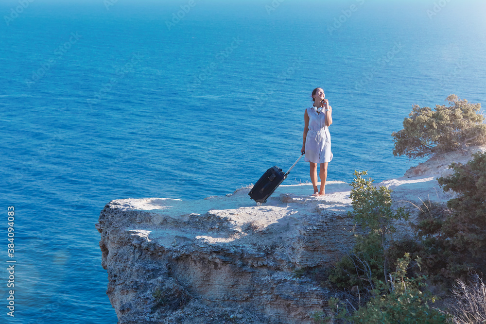 Smiling woman with suitcase posing on sea rock. Seascape on background. Thirst for travel and lifestyle change concept