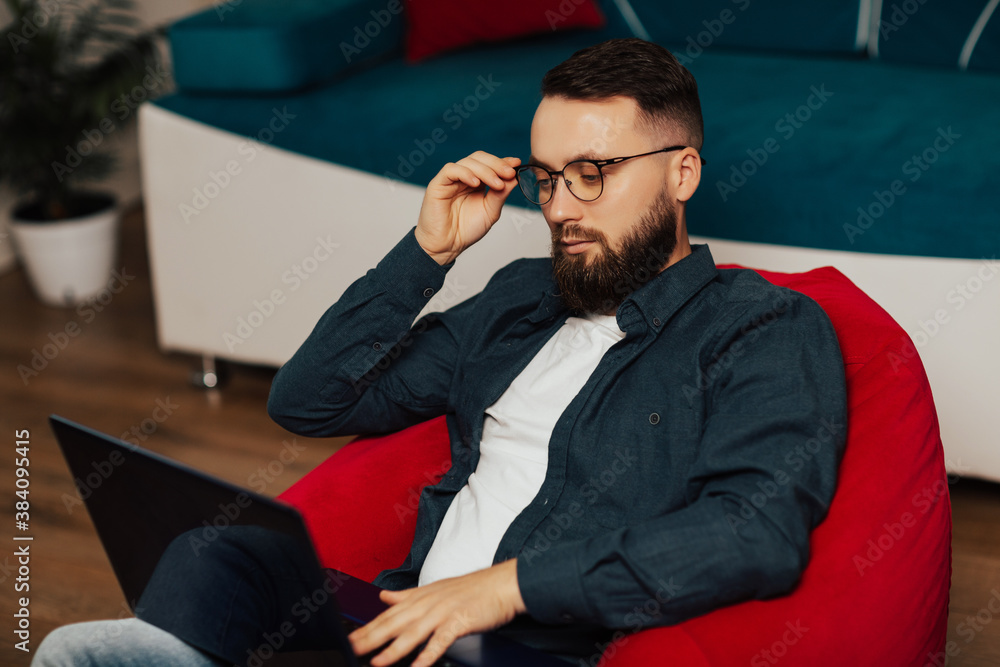 Men wearing blue shirt and eyeglasses using laptop at home office during quarantine. Serious man with glasses thinks while working on laptop at home.