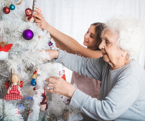 Smiling granddaughter with grandma decorating fancy christmas tree