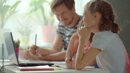 Cute children use laptop for education, online study, home studying, Boy and Girl have homework at distance learning. Lifestyle concept for home schooling. Father helps daughter and son.