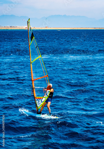 Man spending leisure with extreme windsurfing sport in blue sea with sand beach on background