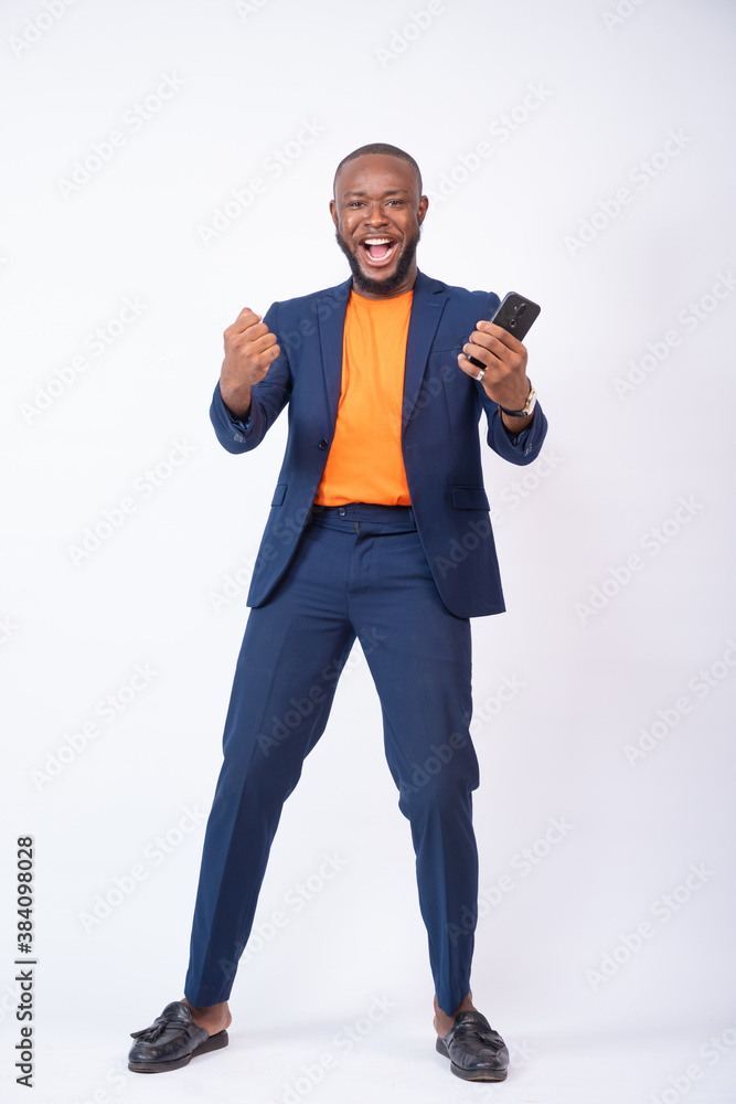 excited african business man celebrating while holding a phone, standing against a white background excited african business man celebrating while holding a phone, standing against a white background