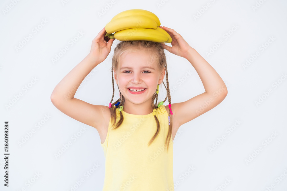 Little smiling girl with banana in yellow shirt on white background