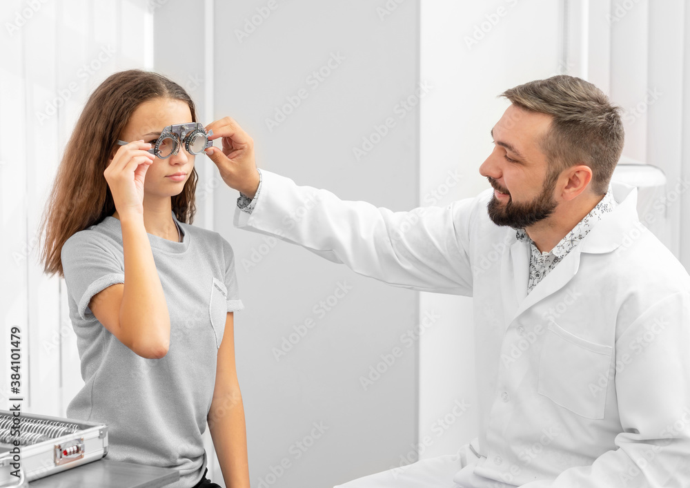 Fototapeta premium Doctor ophthalmologist holding equipment examinating teenager girl's eyes in the clinic