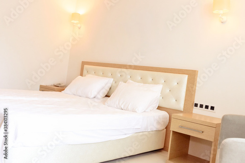 Close up side view of the pillows and headboard of an empty double bed with white and beige linen in the evening.