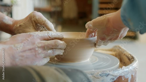 Close-up of two pairs of hands male and female molding pot from clay on throwing wheel working in pottery studio. Relationshop and hobby concept. photo