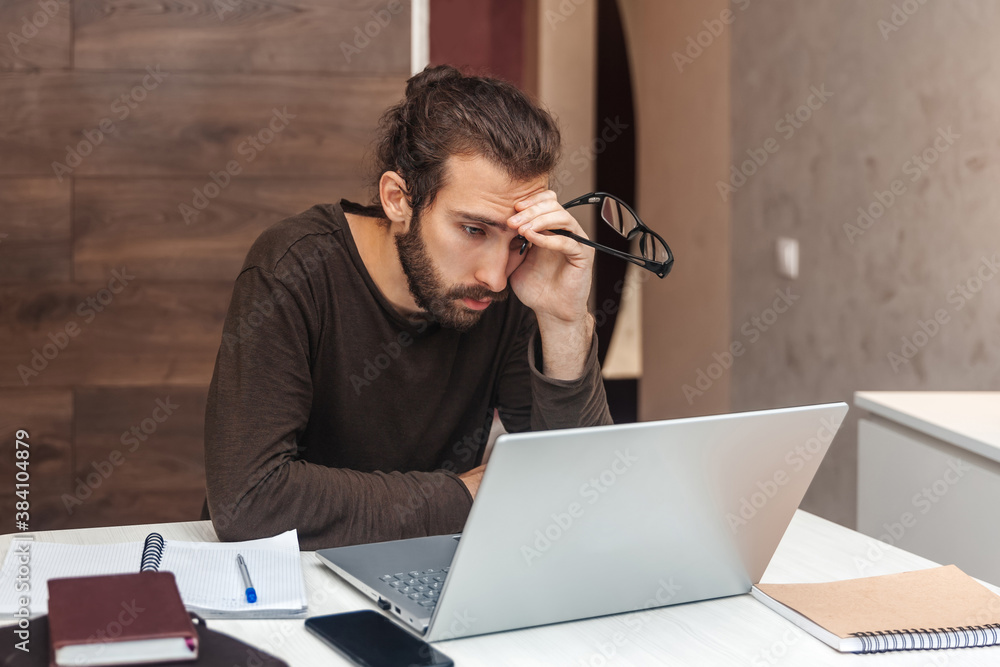 Portrait of a tired programmer. Sad man with beard working at the computer Portrait of a tired programmer. Sad man with beard working at the computer