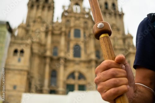 closeup of pilgrim hand holding walking stick with scallop shell, symbol of the camino de santiago pilgrimage, in front of the santiago cathedral