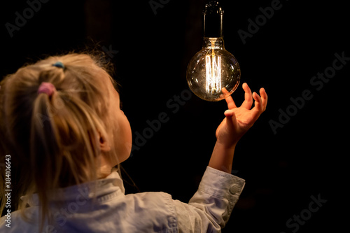 Fotografija Cute adorable caucasian blond girl portrait smiling and holding in hand one of hanged edison light bulb at forest outdoor
