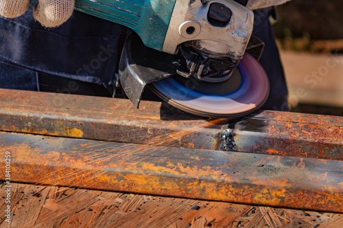 Foto A worker in overalls is grinding a weld seam on a steel square profile pipe with