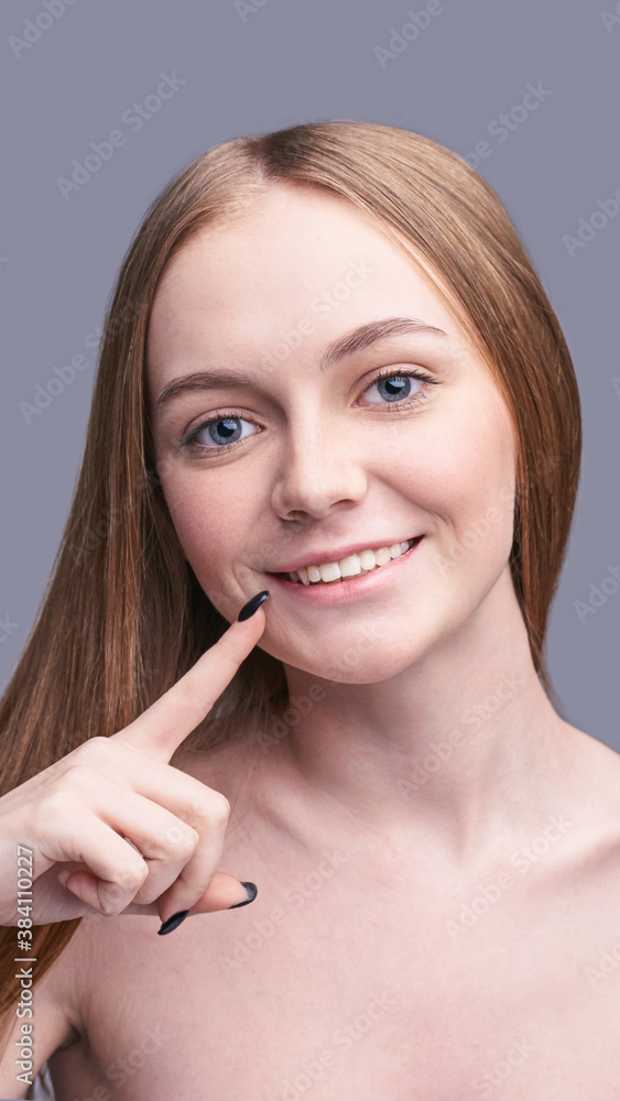Prette girl pointing on smiling mounth. Happy woman portrait. Grey background. Healthy dental beauty. Medical teeth concept. Finger showing model. Cosmetology face Prette girl pointing on smiling mounth. Happy woman portrait. Grey background. Healthy dental beauty. Medical teeth concept. Finger showing model. Cosmetology face