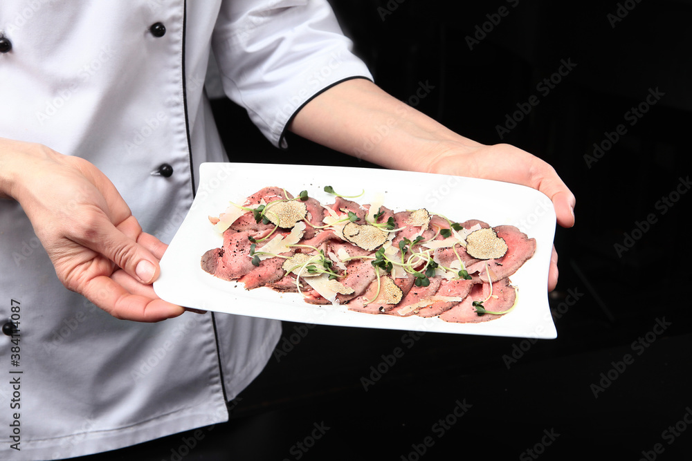 Roast beef with black truffles. The finished dish is in the hands of the chef. Unrecognizable person. Photo on a black background. Top view.