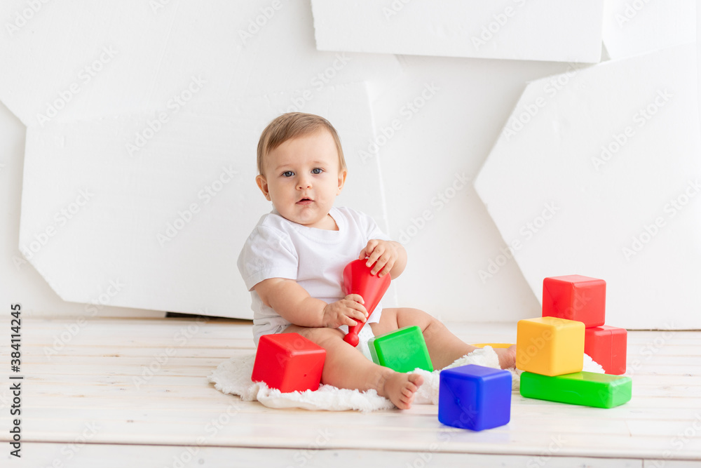 cute little baby six months old in a white t shirt and diapers playing at home on a Mat in a bright room with bright colored cubes cute little baby six months old in a white t shirt and diapers playing at home on a Mat in a bright room with bright colored cubes