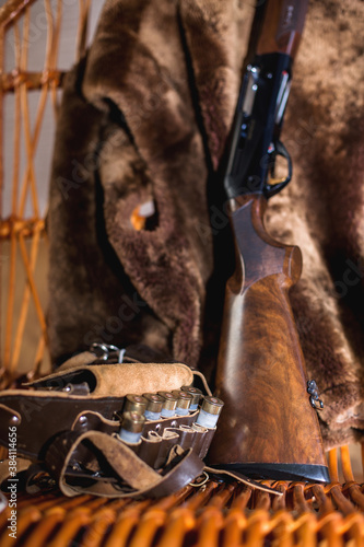 cartridge belt and 12 gauge hunting rifle in a rocking chair. the skin of a bear hangs on the back of a rocking chair