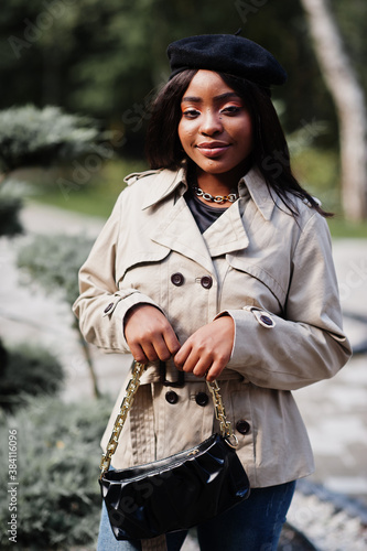 Fashionable african american woman wear beret and coat with handbag posing outdoor.