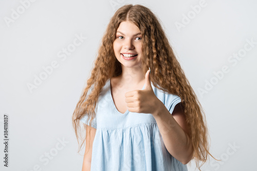 Pretty girl with curly long hair making gesture OK. Studio shot, white background. Human emotions concept