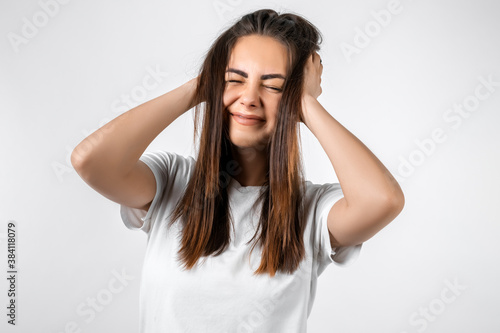 Embarrassed young pretty girl holding her head looking at camera. Studio shot, white background. Human emotions concept © AstiMak