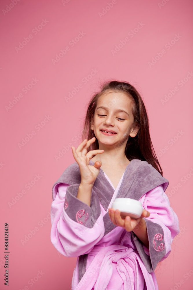 cute girl dressed in a terry bathrobe applies face cream cute girl dressed in a terry bathrobe applies face cream