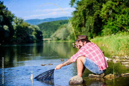 big game fishing. relax on nature. hipster fishing with spoon-bait. fly fish hobby of man. Hipster in checkered shirt. successful fisherman in lake water. mature bearded man with fish on rod