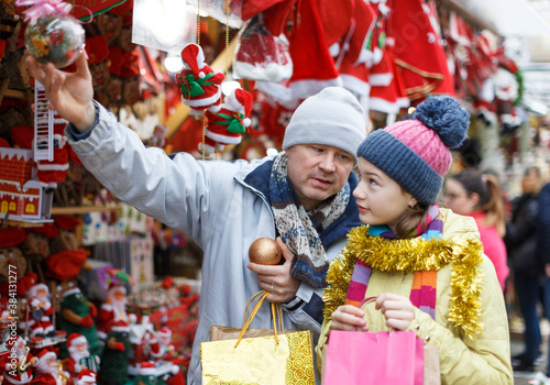 Young father with daughter having fun on Christmas fair, selecting decoration for home..