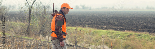 Duck hunter with shotgun walking through a meadow.