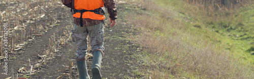 Duck hunter with shotgun walking through a meadow.