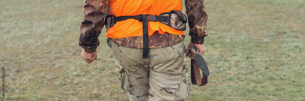 A man with a gun in his hands and an orange vest on a pheasant hunt in a wooded area in cloudy weather. Hunter with dogs in search of game. A man with a gun in his hands and an orange vest on a pheasant hunt in a wooded area in cloudy weather. Hunter with dogs in search of game.
