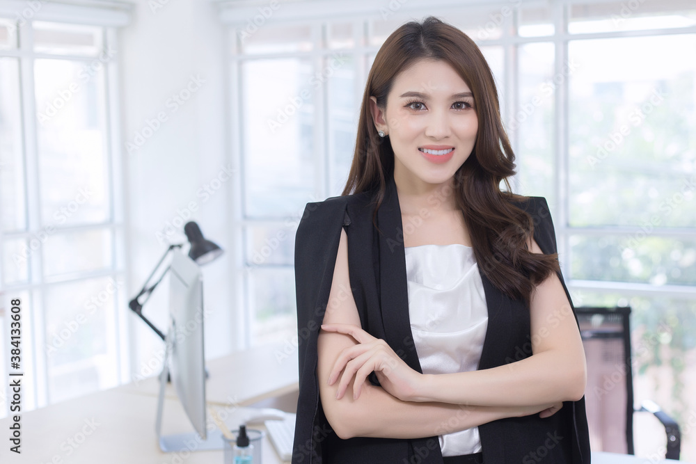 Asian confident woman is standing and arm crossing with smiling face in working room as a background.