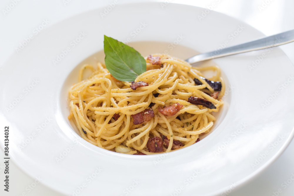 Stir fried spaghetti with dried chilli and crispy bacon  in a white dish.