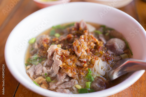 Rice vermicelli (rice noodles) with pork soup contains with meatballs, meat and pickled chili poured on top on woody background.