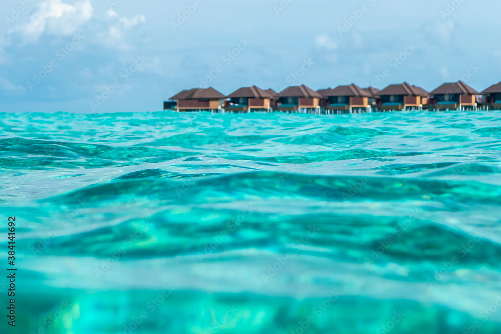 Tropical villas on beach shot from water waves of Indian ocean on Maldive isalnds